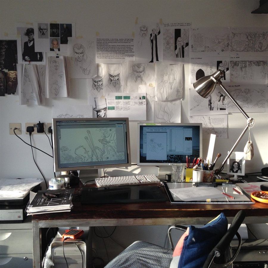 Animator working at a dual-monitor desk surrounded by concept sketches in the Orbital Motion Co. studio